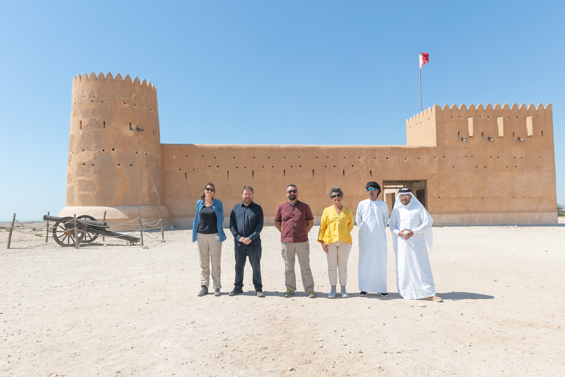 5 people standing facing the camera, in the background is a earthen building 