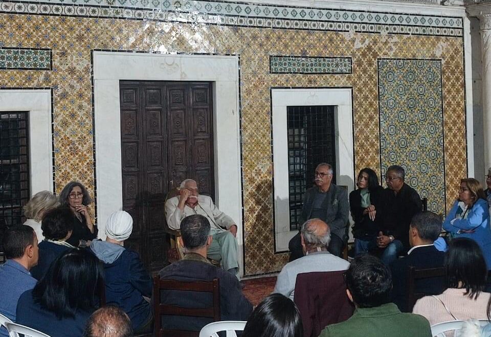 People sitting on chairs in a circle in front of a wall decorated with mosaic tiles
