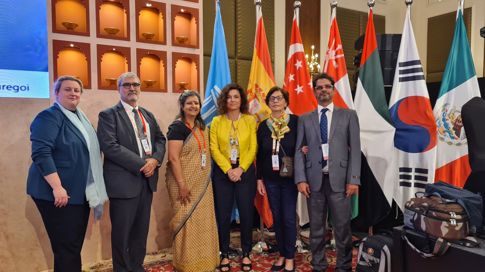 Grouph photo, 6 people smiling and standing in front of various flags.