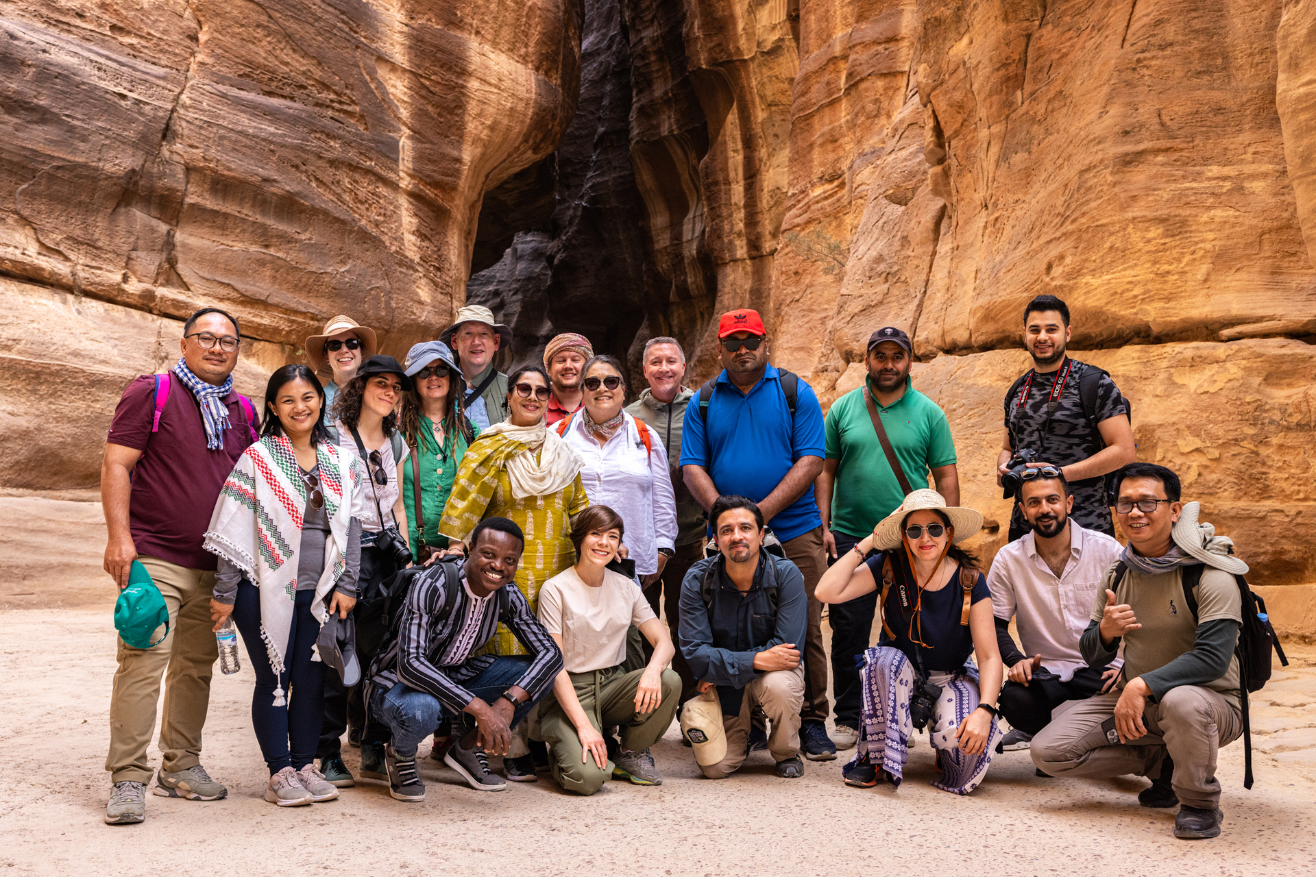 Group of 20 people standing or crouching and smiling at the camera, in front of a canyon background