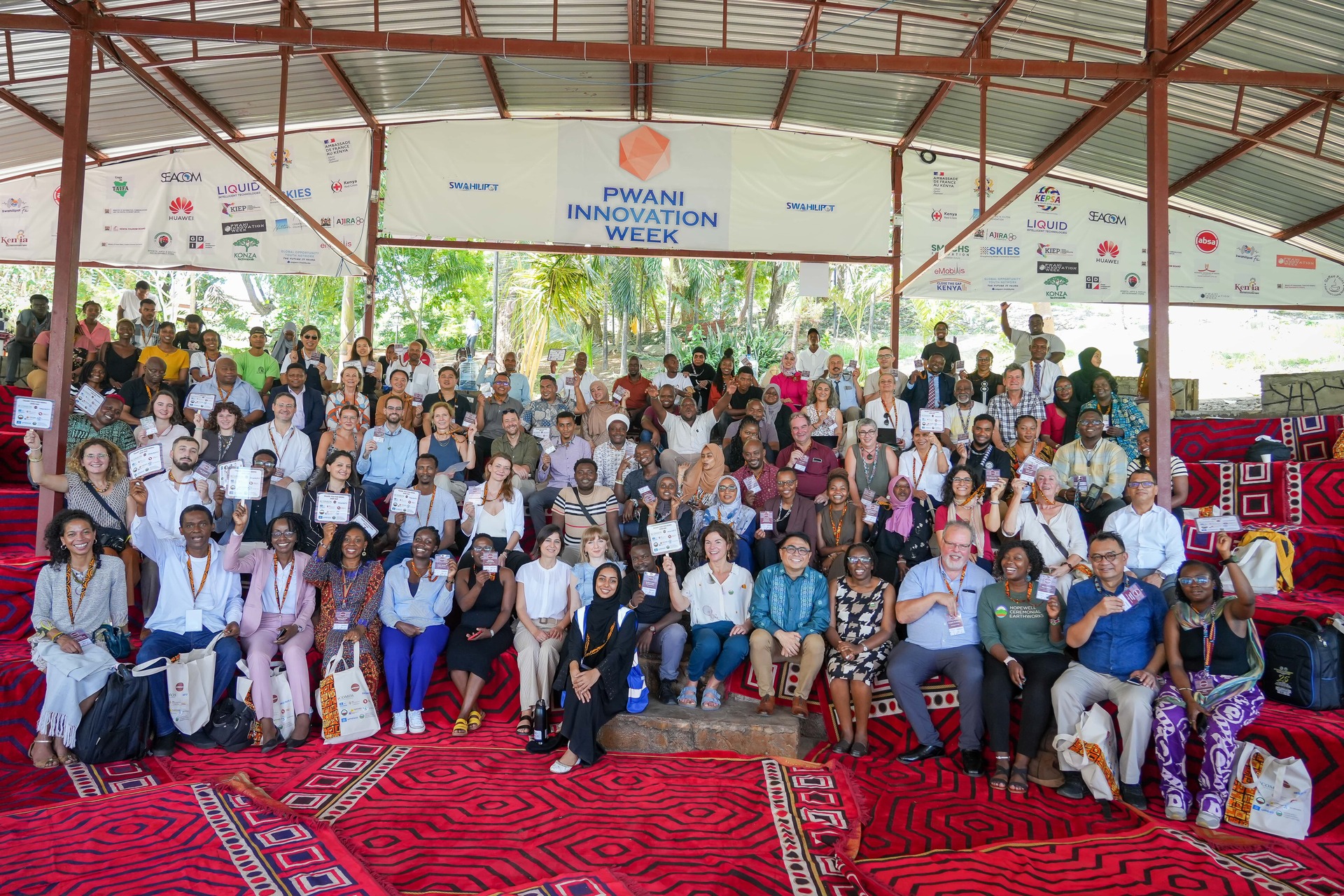 Group of Africa24 participants seated in a small convention venue waving to the camera
