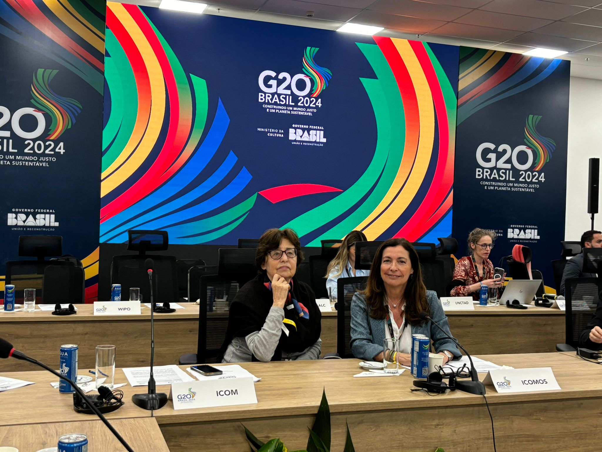 2 women (including ICOMOS president Teresa Patricio) sitting at a table in front of a banner showing the G20 logo