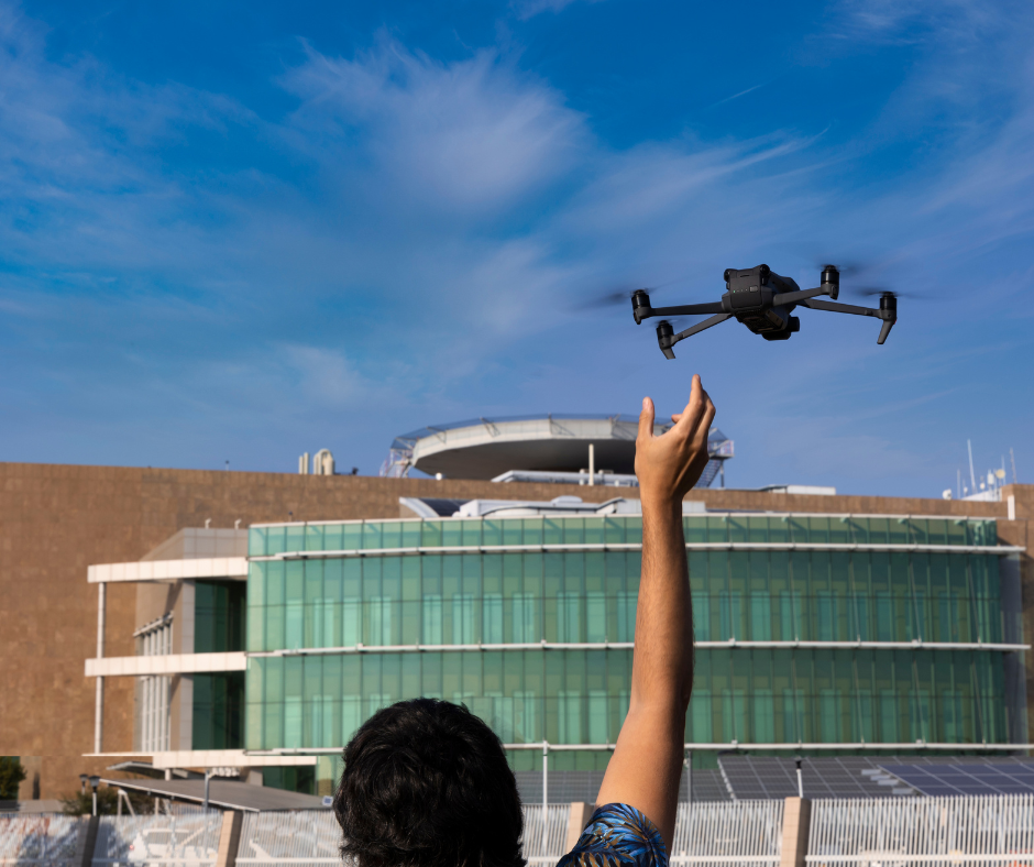 A man flying a drone in front of a brown building with large windows.